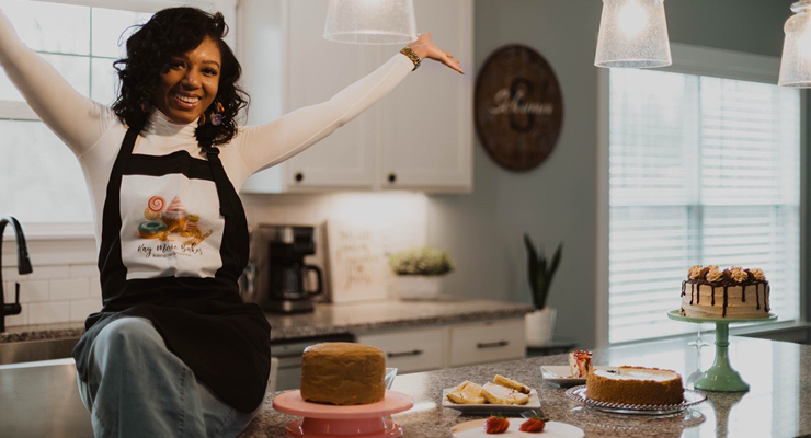 African American woman sitting on a counter surrounded by cakes