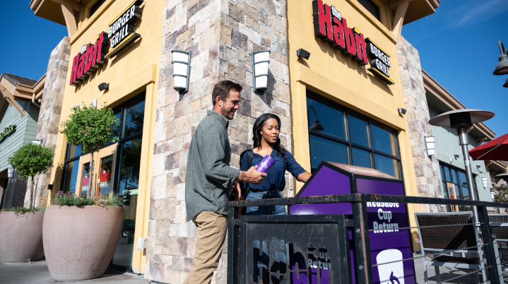 two people returning a cup in front of Habit Burger & Grill