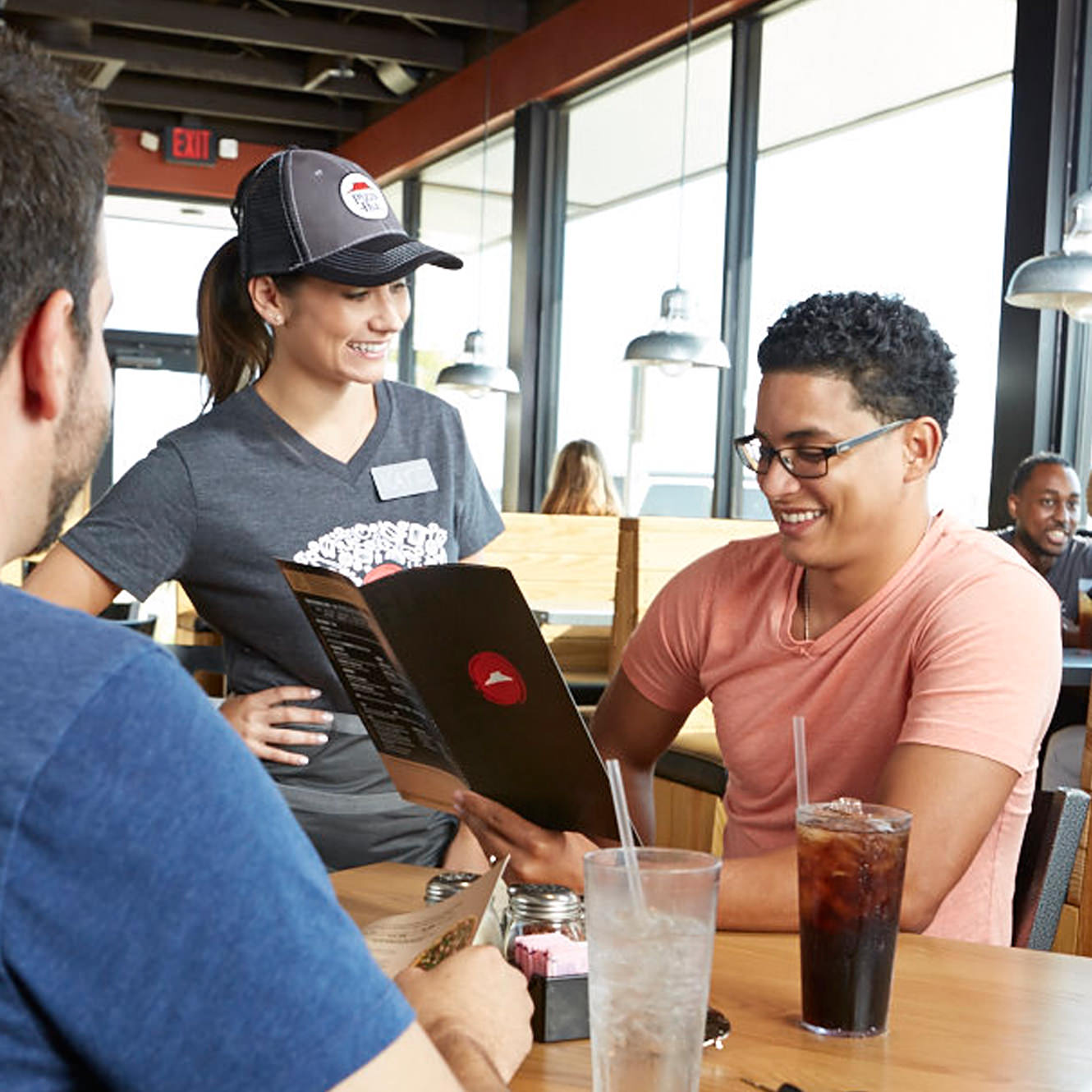 A Pizza Hut associate looks on as a customer seated at a table places an order from a menu A Pizza Hut associate looks on as a customer seated at a table places an order from a menu